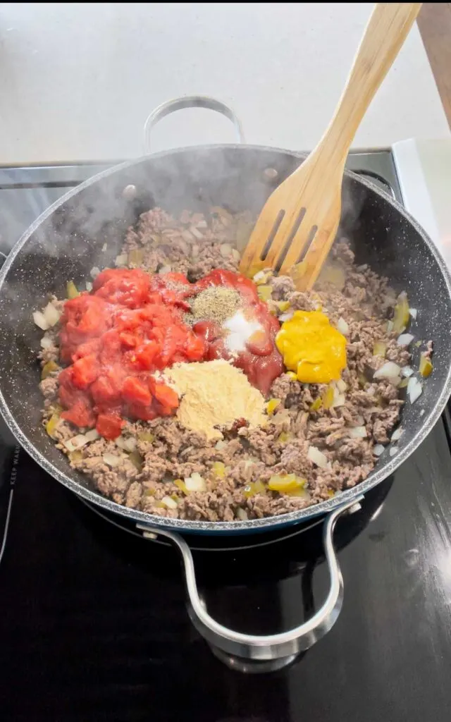 garlic powder, salt, pepper, mustard, ketchup and diced onions on top of cooked ground beef in a skillet